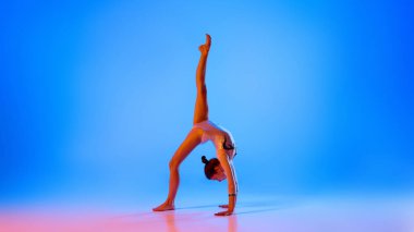 Gücünü ve duruşunu gösteren jimnastikçi kusursuz amuda kalkar. Pembe neon ışıkta, eğimli mavi arka plana karşı. Profesyonel spor anlayışı, aktif yaşam tarzı, hobi. Ad