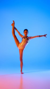 Dayanıklılık ve zarafet. Genç jimnastikçi zarif bir şekilde dengede duruyor, her hareketi pembemsi neon ışığı altında, eğimli mavi arka plana karşı mükemmelleştiriyor. Profesyonel spor anlayışı, aktif yaşam tarzı, hobi. Ad