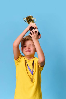 Mutlu, küçük çocuk, klinikte pastel mavi arka plana karşı aşıdan sonra kupa ve madalyayla ayakta duruyor. Sağlık, koruma, dokunulmazlık, önleme kavramı. Reklam. Boşluğu kopyala.
