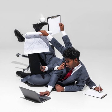 Şirket hayatının acımasız çoklu görev talepleri. Takım elbiseli işadamı, belgeler, telefon ve dizüstü bilgisayar, iş anlayışı, profesyonellik, çoklu görev anlayışı gibi çeşitli ofis araçlarını dengeler. Ad