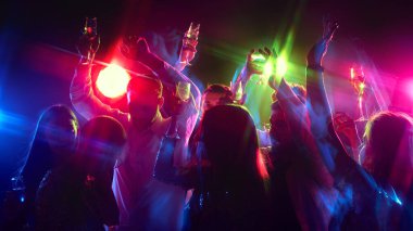 Eller ritim içinde sallanıyor, kalabalık hayatı, müziği kutlarken bardaklar tokuşturuyor ve neon ışıkları altında mutluluğu paylaşıyor. İş partisi, gençlik, tasasız, kutlama, kış tatili. ad