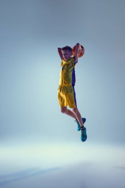 Küçük atletik çocuk, basketbolcu gri stüdyo arka planına güçlü bir smaç basmak için havada atlıyor. Spor anlayışı, eğlence aktivitesi, hobi, rekabet. Ad
