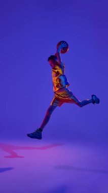 Nihai hedef. Oyuna odaklanmış, kendine güvenen genç basketbolcu, neon ışıkta hareketli bir şekilde stüdyonun arka planına doğru sıçrıyor. Spor anlayışı, eğlence aktivitesi, hobi, rekabet. Ad