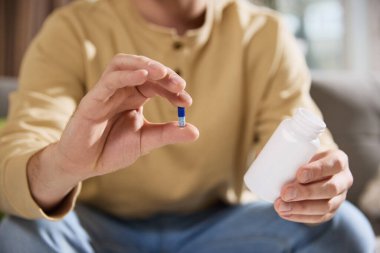 Bir elinde vitamin ya da diyet takviyeleriyle dolu, diğer elinde kapsül bulunan, erkek eli kavanozunun kesilmiş fotoğrafı. Hastalık kavramı, sağlık sigortası, tıp. Ad.