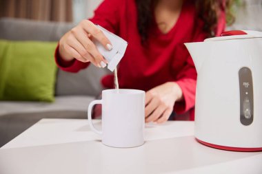Kadın, evdeki oturma odasındaki masaya koyduğu beyaz bardağa, içinde negatif boşluk olan kese dolduruyor. Hastalık kavramı, sağlık sigortası, ilaç, ilaç. Ad.