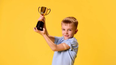 Kolunda ilaç bandıyla altın kupa kaldıran mutlu çocuk sarı stüdyo geçmişine karşı güven ve heyecan gösteriyor. Sağlık, koruma, dokunulmazlık, önleme kavramı.