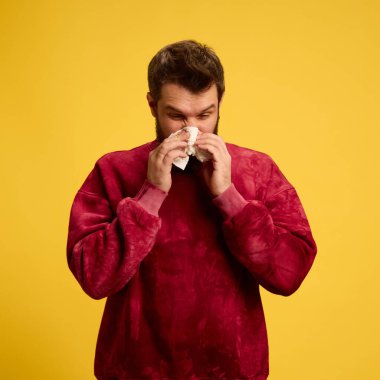 Alerjiden muzdarip sıradan giyinen genç bir adam sarı stüdyo arka planında akan bir burnu var. Sağlık, ilaç, virüs, enfeksiyon ve tedavi kavramı. Ad.