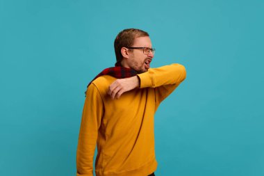 Gözlüklü sıradan giyinen bir adam mavi stüdyo geçmişine karşı alerji, hapşırma ve öksürükten muzdarip. Sağlık, ilaç, enfeksiyon ve tedavi kavramı. Ad.