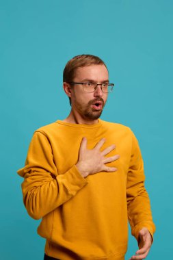 Mavi stüdyo arka planında sarı süveter ve gözlük giymiş, göğsü açık el ele tutuşan bir adam. Sağlık, ilaç, enfeksiyon ve tedavi kavramı. Ad.