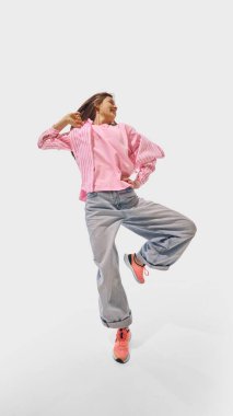 Pembe ve kot elbiseler içinde dans eden kadın, beyaz stüdyo geçmişine karşı neşe ve güven saçıyor. Başarı kavramı, profesyonel gelişme, hareket. Ad