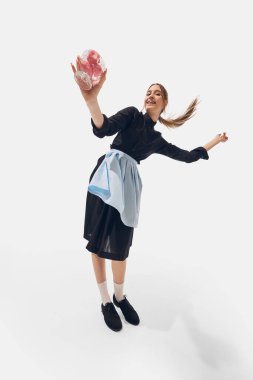 Siyah ve mavi üniformalı bayan garson, beyaz stüdyo arka planında pembe tatlı tutarken hafifçe dönüyor. Geniş açı. Başarı kavramı, mesleki gelişim, hareket