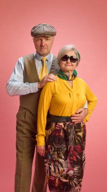 Ciddi ifadeleri olan olgun bir erkek kadının omzunda kameraya bakıyor. Yeşil fularlı ve güneş gözlüklü kadın kendinden emin poz veriyor. Olgun insanlar ve moda kavramı. Ad