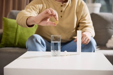 Cropped photo of man put soluble vitamin tablet to glass of clean water that is on table in living room at home. Concept of illness, healthy insurance, pharmaceutical, medicine. Ad. clipart