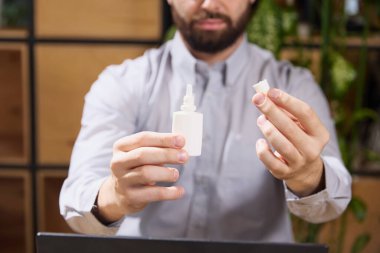 Genç adam iş yerinde oturur ve bir şişe burun spreyi açar. Mesajını eklemek için içinde negatif boşluk vardır. Seçici odaklı fotoğraf. Hastalık kavramı, sağlık sigortası, ilaç, ilaç. Ad.