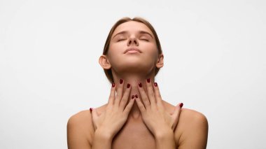 Genç bir kadın. Başını arkaya eğiyor, boynuna dokunuyor ve beyaz stüdyo arka planına masaj yapıyor. Tedaviyi kaldırıyorum. Doğal güzellik kavramı, kişisel bakım, cilt bakımı. Ad