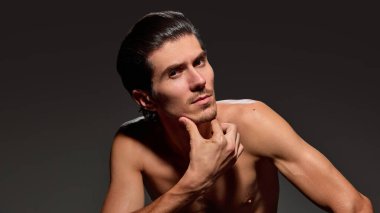 Yakışıklı, şık bir adam çenesini elinde dinlendirip kendine güvenen bir poz veriyor, koyu arkaplanda odaklanmış ifadesini vurguluyor. Erkek güzelliği ve yüz bakımı kavramı, yaşlanma karşıtı prosedürler.