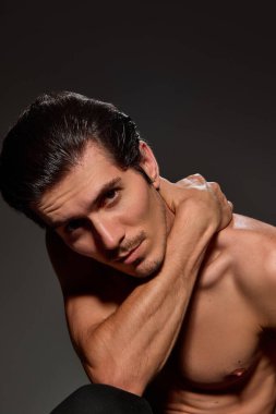 Bir adam başını hafifçe eğiyor, bir kolu omzunda dinleniyor. Kendine güveni ve parlak saç stili koyu arkaplana vurgu yapıyordu. Erkek güzelliği ve yüz bakımı prosedürleri kavramı.