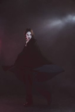 Siyah pelerin giymiş bir adam, vampir, dumanla dolu bir çevrede yoğun bir ifadeyle loş ışık altında hareket ediyor. Tarihsel ve modernlik kavramı, moda ve tarz, yaratıcılık.