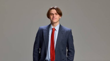 Güvenle ayakta duran genç adam, temiz gri stüdyo geçmişine karşı donanma takımı ve kırmızı kravat da dahil olmak üzere iş kıyafetlerini sergiliyor. İnsani duygular, kendini ifade etme, moda ve tarz kavramı. Ad