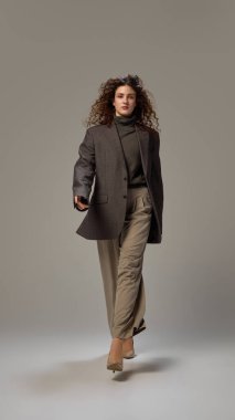 Çekici genç bir bayanın dinamik fotoğrafı, Pastel renk düzeniyle resmi giyinmiş, gri stüdyo arka planına karşı hareket halinde. İnsan duyguları, kendini ifade etme, moda ve tarz kavramı.