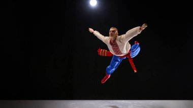 Zengin detaylı Ukrayna kıyafeti içinde halk dansçısı, geniş bir gülümseme ile dönüş ortasında yakalandı, Hopak içinde karanlık arka plana karşı canlı hikaye anlatımı canlandırıyor. Gelenek, sanat ve tarih kavramı.