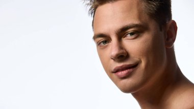 Islak saçlı, kendine güvenen, beyaz arka planda hafif bir gülümsemeyle kameraya bakan çekici bir adam. İyi korunmuş ciltli bir erkek model. Bencillik kavramı, doğal güzellik, kozmetoloji.