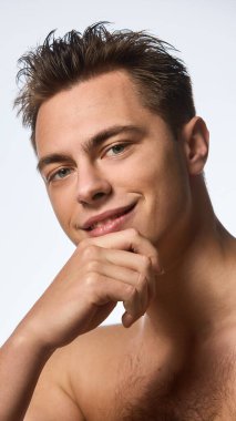 Yakından, ıslak saçlı genç bir adamın beyaz stüdyo arka planında el ele tutuşup kameraya baktığı bir fotoğraf. Bencillik ve sevgi kavramı, doğal güzellik, kozmetoloji.