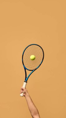El sıkışan tenis raketi, havada beliren sarı top, doğruluğu sembolize ediyor, ve sıcak tonlu arka plana güçlü bir atış yapmadan önceki an. Spor aletleri, kontrol ve strateji kavramı. Ad