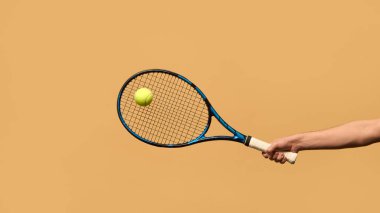 Uzamış kollar tenis raketini tutuyor, top önde uçuyor, konsantrasyonu, zamanlamayı ve sıcak tonlu arka plana uygulanan mükemmel darbeyi temsil ediyor. Spor malzemesi kavramı, strateji.