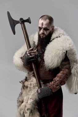 Sakallı adam, ortaçağ savaşçısı deri ve kürklü giysiler içinde elinde baltayla şiddetli bir savaşa hazır olduğunu gösteriyor. Viking efsaneleri. Tarihi portre kavramı. Kitap ve film kapakları