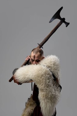 Ortaçağ Viking savaşçısı kürk pelerinli ve zırhlı, iki elinde kocaman baltayla stüdyonun arka planına şiddetle saldırmaya hazır. Tarihi portre kavramı