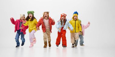 Renkli kışlık ceketler ve şapkalar giymiş bir grup çocuk heyecanlı ifadelerle öne doğru koşuyor, beyaz stüdyo geçmişine karşı neşe ve enerji gösteriyorlar. Çocukluk kavramı, kış tatili