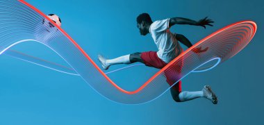 Spor kolajı. Futbol sporcusu hareket girdaplarıyla havada tekme atıyor. Derin mavi eğimli arka plana çarptığını vurguluyor. Spor anlayışı, takım çalışması, yetenek, nihai amaç.