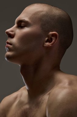 Yan profilde odaklanmış erkek yüzü pürüzsüz bir ten ve kahverengi arka plana yoğun bir bakışla bakıyor. Güç, güven, erkeksilik, doğal güzellik, estetik, anlamlı derinlik kavramı.