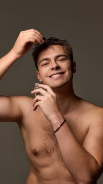 Adam serumu damlatırken gülümsüyor, diğer elinde şişe tutuyor, kahverengi stüdyo arka planında kameraya bakıyor. Bencillik ve sevgi kavramı, doğal güzellik, kozmetoloji.