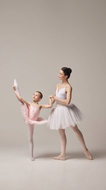 Pembe etekli küçük balerin bir bacağının üzerinde kollarını uzatır ve annesi ona yardım eder, bej arka planda konsantrasyon ve zarafet gösterir. Bale kavramı, zarafet ve güzellik, zarafet..