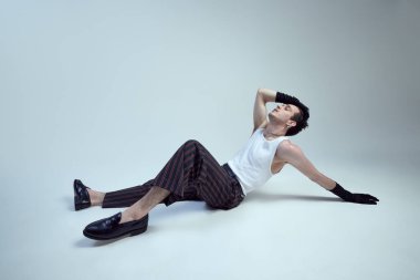 Genç adam şık giyinmiş, yüksek moda karizması yayıyor heykel şeklinde ve gradyan arka planda çarpıcı bir silueti var. Güzellik kavramı, moda ve tarz, kendini ifade etme.