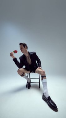 Kendine güvenen genç bir adam, taburede oturuyor şık bir duruşu ve beyaz stüdyo arka planına karşı şık bir modası olan gülü hayranlıkla seyrediyor. Güzellik kavramı, moda ve tarz, kendini ifade etme.