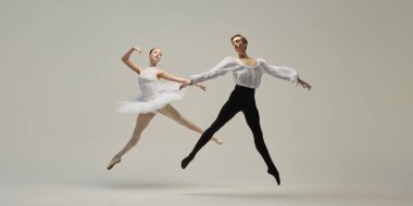 Genç bale dansçılarının dinamik fotoğrafı, esnek vücutları beyaz stüdyo arka planına ters yönlere dönük. Klasik konsept, kontrast, zarafet, hareket.