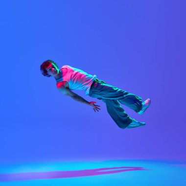 Yetenekli break dansçı, yer çekimine meydan okuyarak neon ışıklı mavi mor renge karşı hareketler yapıyor. Sokak performansı, hip-hop kültürü, kendini ifade etme, enerji ve hareket kavramı.