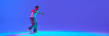 Günlük kıyafetlerle dans eden genç bir adamın dinamik görüntüsü. Neon ışıkta, değişken mavi arka planda hip-hop yapıyor. Dans kavramı, sokak tarzı, yaratıcılık, gençlik kültürü, enerji. Boşluğu kopyala