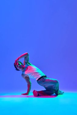 Atletik genç adam serbest dans yetenekleri sergiliyor, neon ışıkta mavi renkli arka plana karşı güç ve ritim yayıyor. Dans, tutku, kendini ifade ve hareket kavramı.