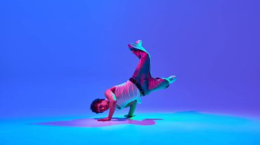 Dönüşün ortasında yetenekli hip-hop dansçısı, dengeleme tekniği ve ritmi neon ışıkta değişen mavi arkaplana karşı. Dans kavramı, sokak tarzı, yaratıcılık, gençlik kültürü, enerji