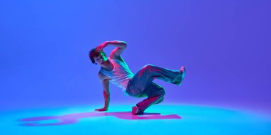 Yetenekli ve yetenekli genç adam hareketli gündelik giysiler içinde, neon ışıkta mavi renkli arka planda dans ediyor. Serbest stil kavramı, yaratıcılık, modern dans hareketi.