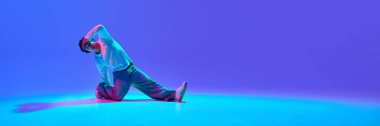 Limitleri aşan güçlü genç dansçı, neon ışıklarıyla gradyan mavi arkaplana karşı dinamik break dans yapıyor. Dans kavramı, sokak tarzı, yaratıcılık, gençlik kültürü, enerji