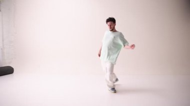 Gündelik giyinmiş, aşırı şık giyinmiş, beyaz stüdyo geçmişine karşı serbest dans eden genç bir sanatçı. Sanat ve spor kavramı, müzik, yaratıcılık, moda ve tarz.