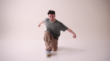 Yetenekli dansçı, sokak tarzı giyinmiş genç atletik adam ve beyaz stüdyo geçmişine karşı müzik ritmiyle hareket ediyor. Sanat ve spor kavramı, müzik, yaratıcılık, moda ve tarz.