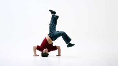 Breakdansçı, beyaz arka planda amuda kalkıyor, gövdesi kavisli, tek bacağı yüksek, gücü ve dengesi yerinde. Sanat kavramı, kendini ifade etme, dayanıklılık, hareket, yaratıcılık.