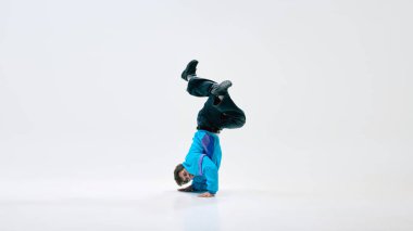 Dansçı, şık giyinmiş, klasik kıyafetler giymiş, amuda kalkmış, bacakları beyaz arka planda bükülmüş. Kontrollü hareket. Vücut gücü kavramı, dans kültürü, spor, esneklik, break dans.