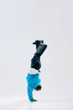 Genç break dansçı beyaz arka planda dengede duruyor. Tüm vücut kontrolü hareketi ifade ediyor. Spor, dans, ritim, öz disiplin, serbest hareket, çağdaş sanat kavramı.